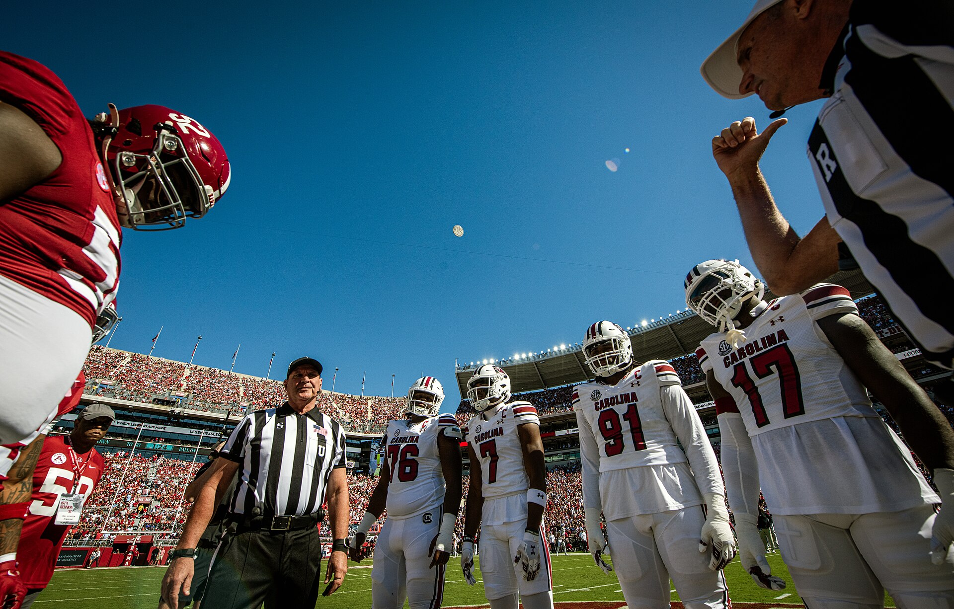 Team captains and referees watch the coin flip in midair before a packed college football game