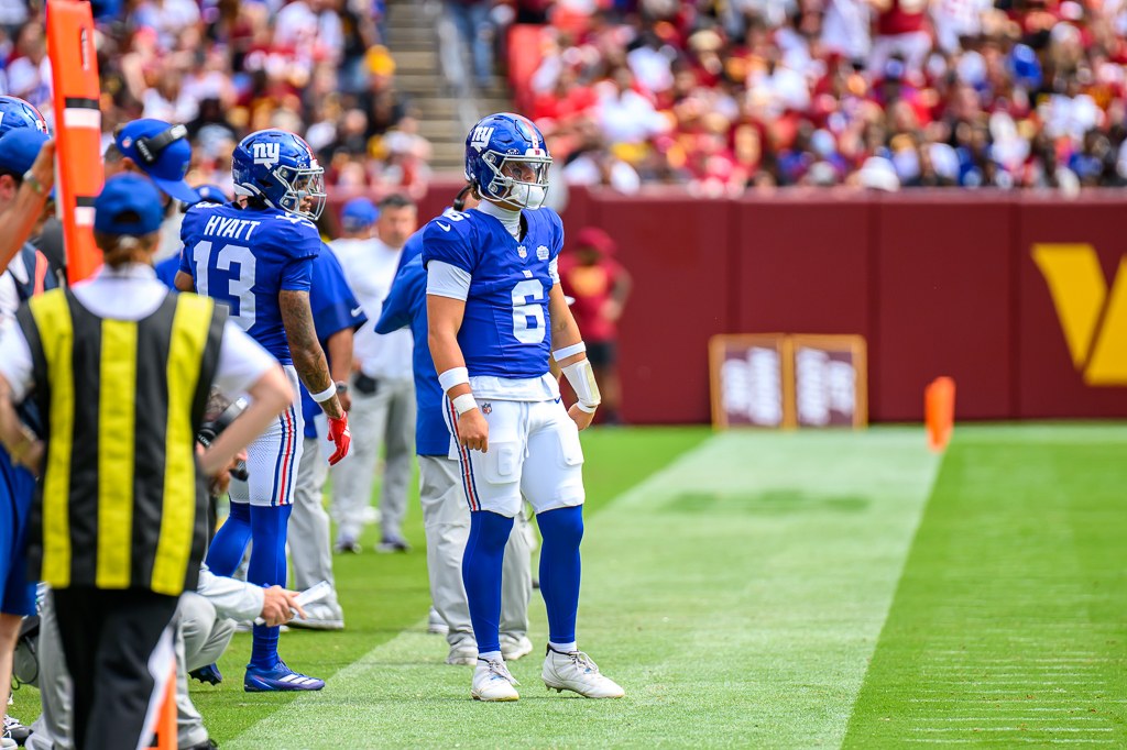Jaxson Dart standing on the Giants sideline in a blue number 6 jersey during a 2025 game