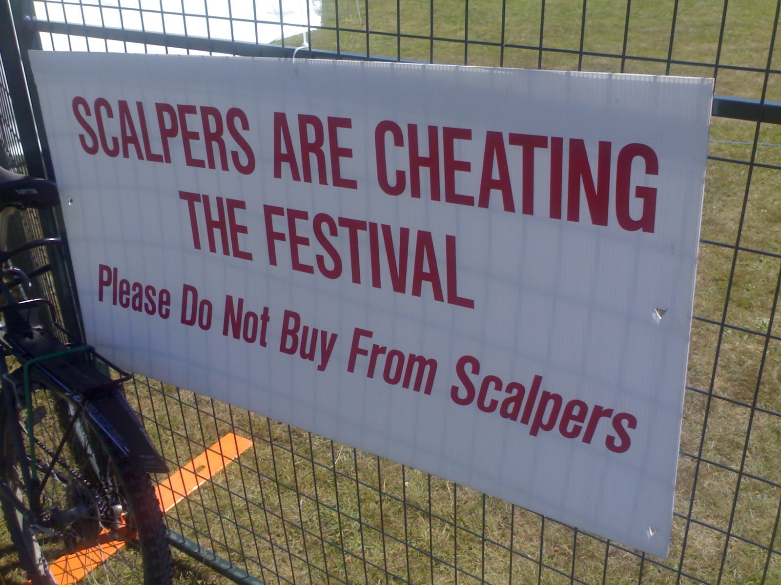A sign on a festival fence reading Scalpers Are Cheating The Festival, Please Do Not Buy From Scalpers